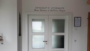 Una puerta blanca con paneles de vidrio esmerilado y un picaporte de metal. Sobre la puerta, hay una placa con coordenadas y el nombre "Haus Hannes en Mellnitz/Rügen".