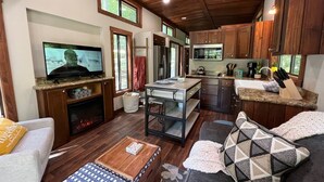 Un salon chaleureux avec une cheminée, un téléviseur et un coin cuisine doté de meubles en bois et d’un plan de travail.