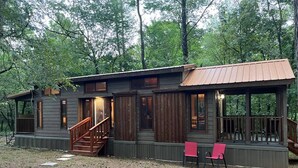 Une cabane avec une façade en bois, une véranda dotée de deux chaises rouges et un escalier menant à l’entrée.