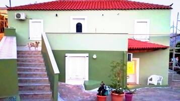 A two-story house with a red-tiled roof, a staircase leading to the upper floor, and a small porch area with potted plants.