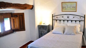 Une chambre à coucher avec un lit, des poutres en bois, une fenêtre, une table de chevet et un tableau accroché au mur.