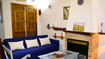 A living room with a blue sofa, a glass coffee table, a fireplace, and a wooden door.