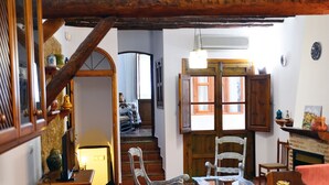 Un intérieur rustique avec des poutres en bois, un escalier, un coin repas avec des chaises et une cheminée.