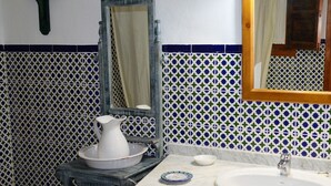 Une salle de bain avec un lavabo, un miroir et un pichet posé sur une petite table.