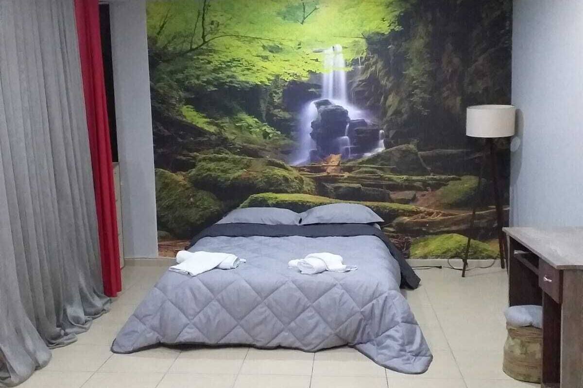 Un dormitorio con cama, un mural de una cascada, una lámpara y una cortina.