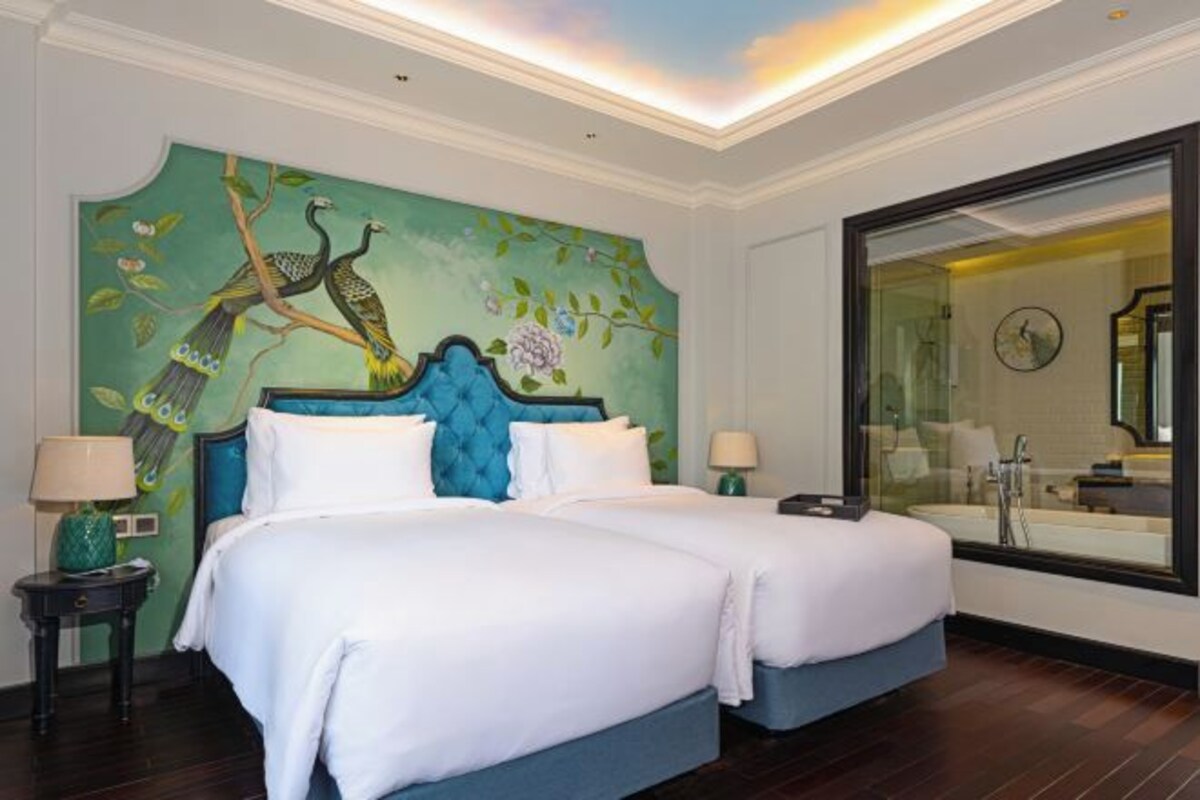 Quarto de hotel com duas camas, um espelho grande e um mural de pássaros na parede.