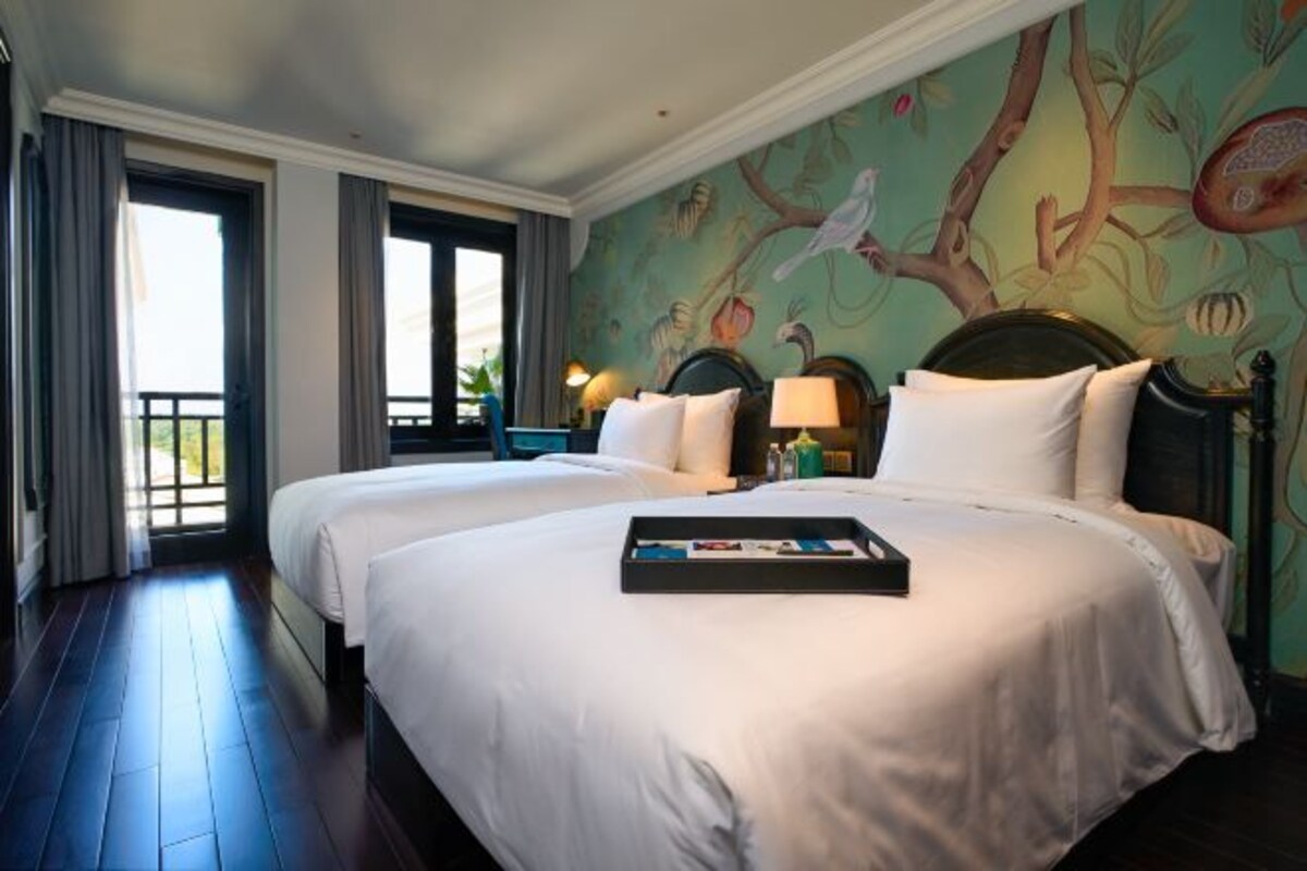 Quarto de hotel com duas camas, um mural na parede e vista para o exterior.
