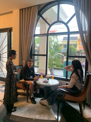 A room with a large arched window, a round table with drinks, and a view of buildings and greenery outside.