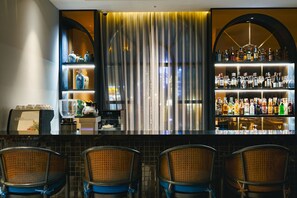 A bar area with a counter, shelves of bottles, and chairs.