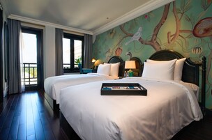 Habitación de hotel con dos camas, un mural de pájaros en la pared y una bandeja con fotografías sobre la cama.