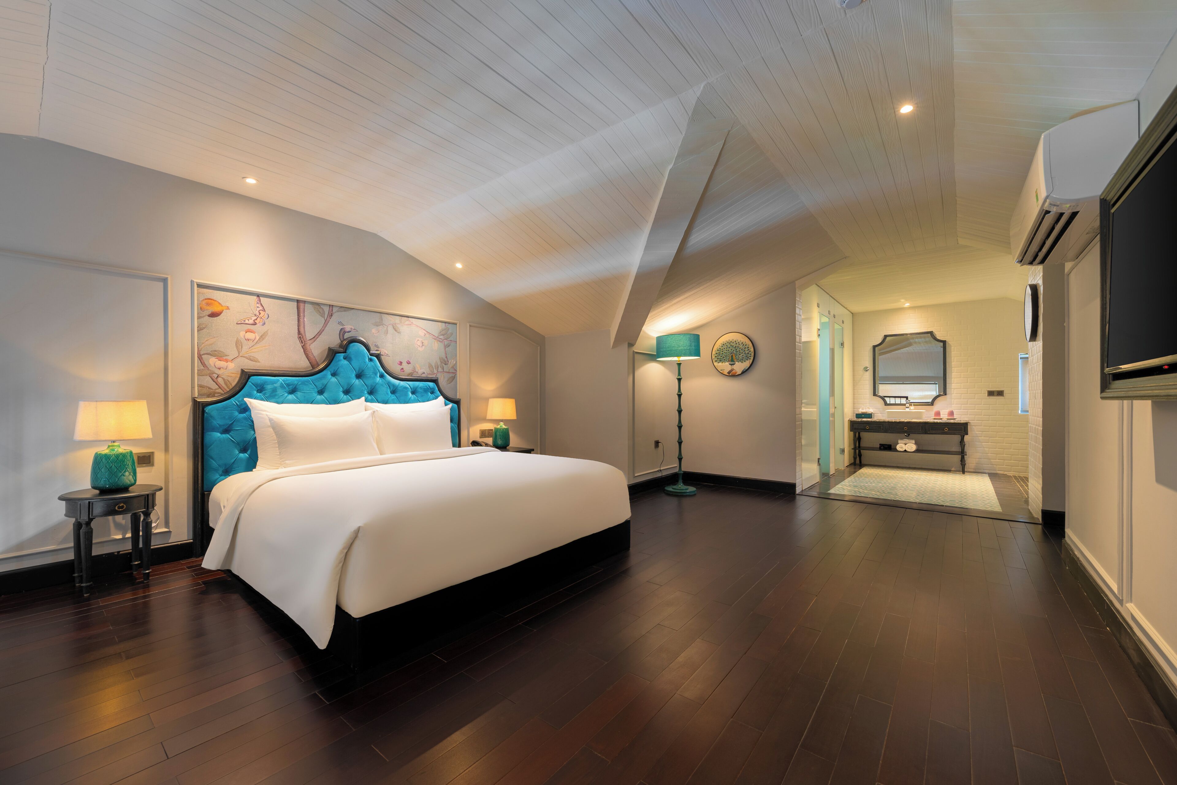 A spacious bedroom with a large bed, a decorative headboard, a nightstand, a lamp, and a wall-mounted TV.