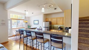 Une cuisine moderne dotée d’un îlot central, de tabourets de bar, de meubles en bois et d’un réfrigérateur en acier inoxydable.