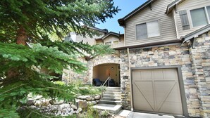 Une maison d’habitation avec une façade en pierre, un garage et un petit porche doté d’un espace salon extérieur.
