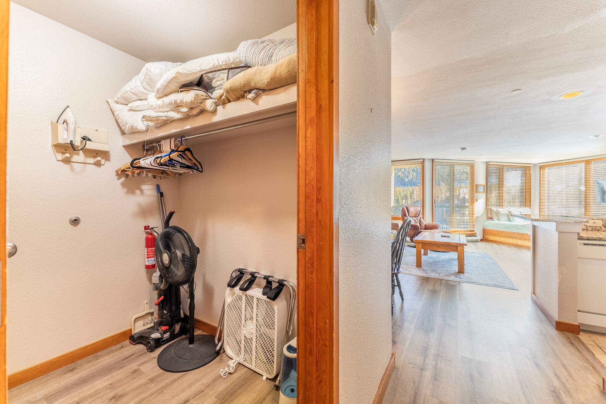 A compact hotel room with a bunk bed, a small closet, a heater, a fan, and a view of the living area through large windows.