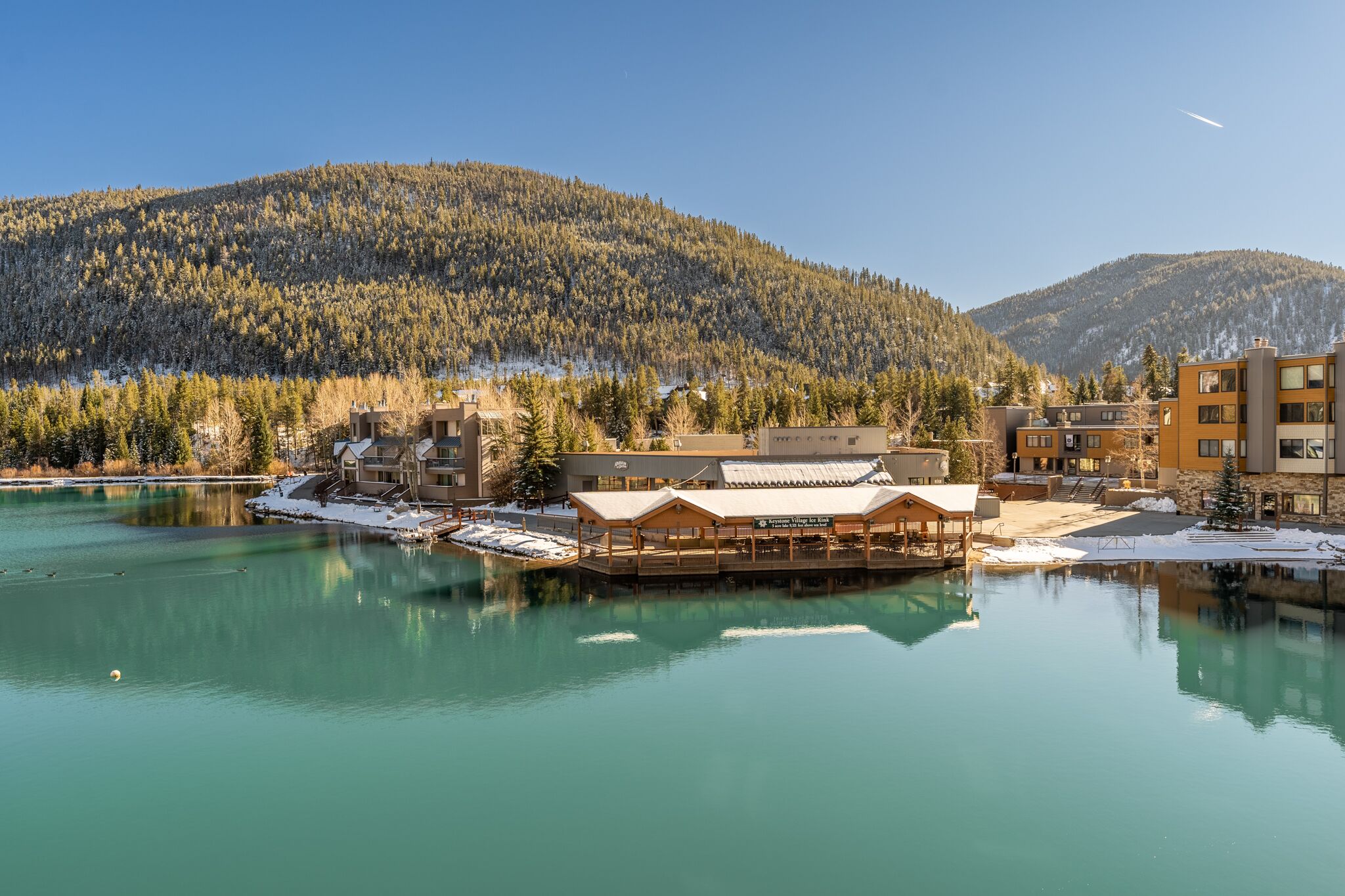 Un chalet au bord du lac, doté d’une terrasse en bois et offrant une vue sur une montagne boisée.