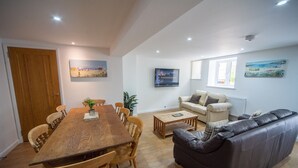 A spacious living room with a wooden dining table, leather sofa, and a television mounted on the wall. - Luxury 2 bed apartment a few minutes walk from beach, harbour and town! (Torquay)