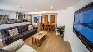 A modern living room with a brown leather sofa, a wooden coffee table, and a dining area with a wooden table and chairs. - Luxury 2 bed apartment a few minutes walk from beach, harbour and town! (Torquay)