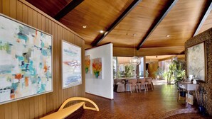 A spacious lobby with wooden paneling, artwork on the walls, a curved bench, and a dining area in the background.