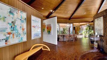 Um hall espaçoso com lambris, obras de arte nas paredes, um banco curvo e uma área de refeições ao fundo.
