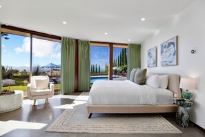 A bedroom with a large bed, a view of a swimming pool, and a chair by the window.