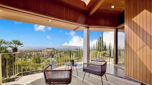A balcony with two chairs and a table, overlooking a scenic landscape with trees and mountains.