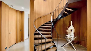 A modern spiral staircase with wooden walls and a glass table with a sculpture.