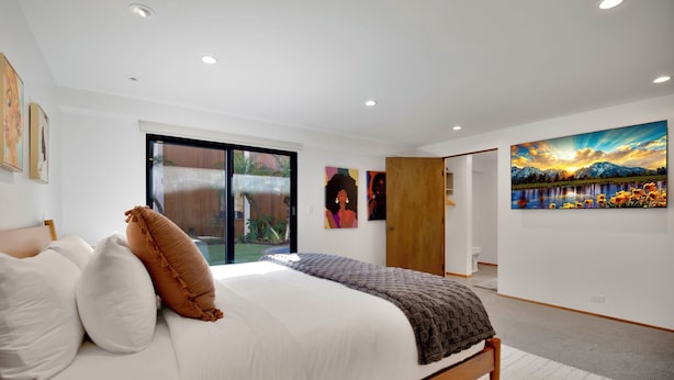 A bedroom with a bed, a large window, and artwork on the walls.