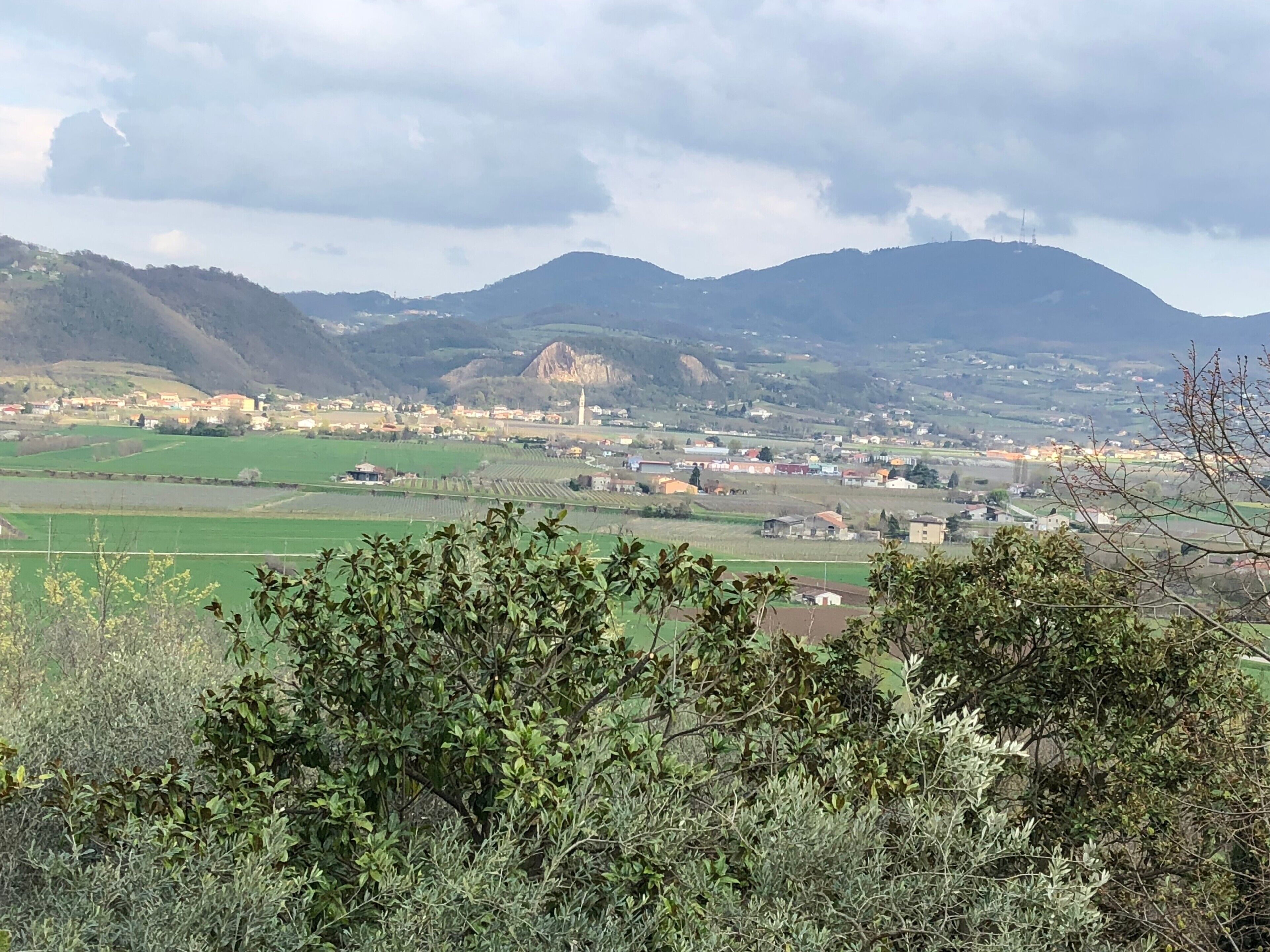 Paesaggio rurale con campi, un piccolo paese e montagne sullo sfondo.