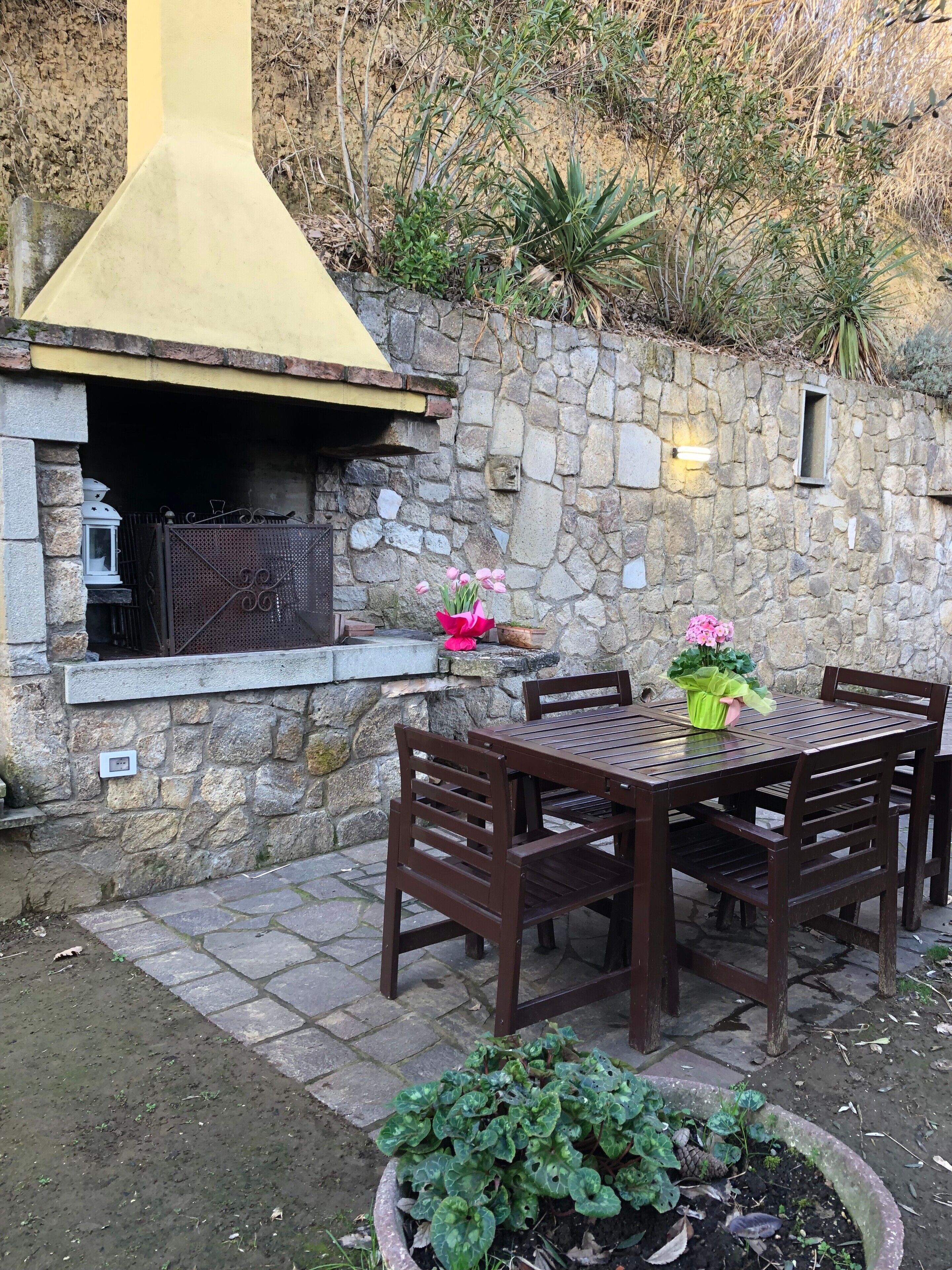 An outdoor patio with a stone wall, a grill, and a table with chairs.
