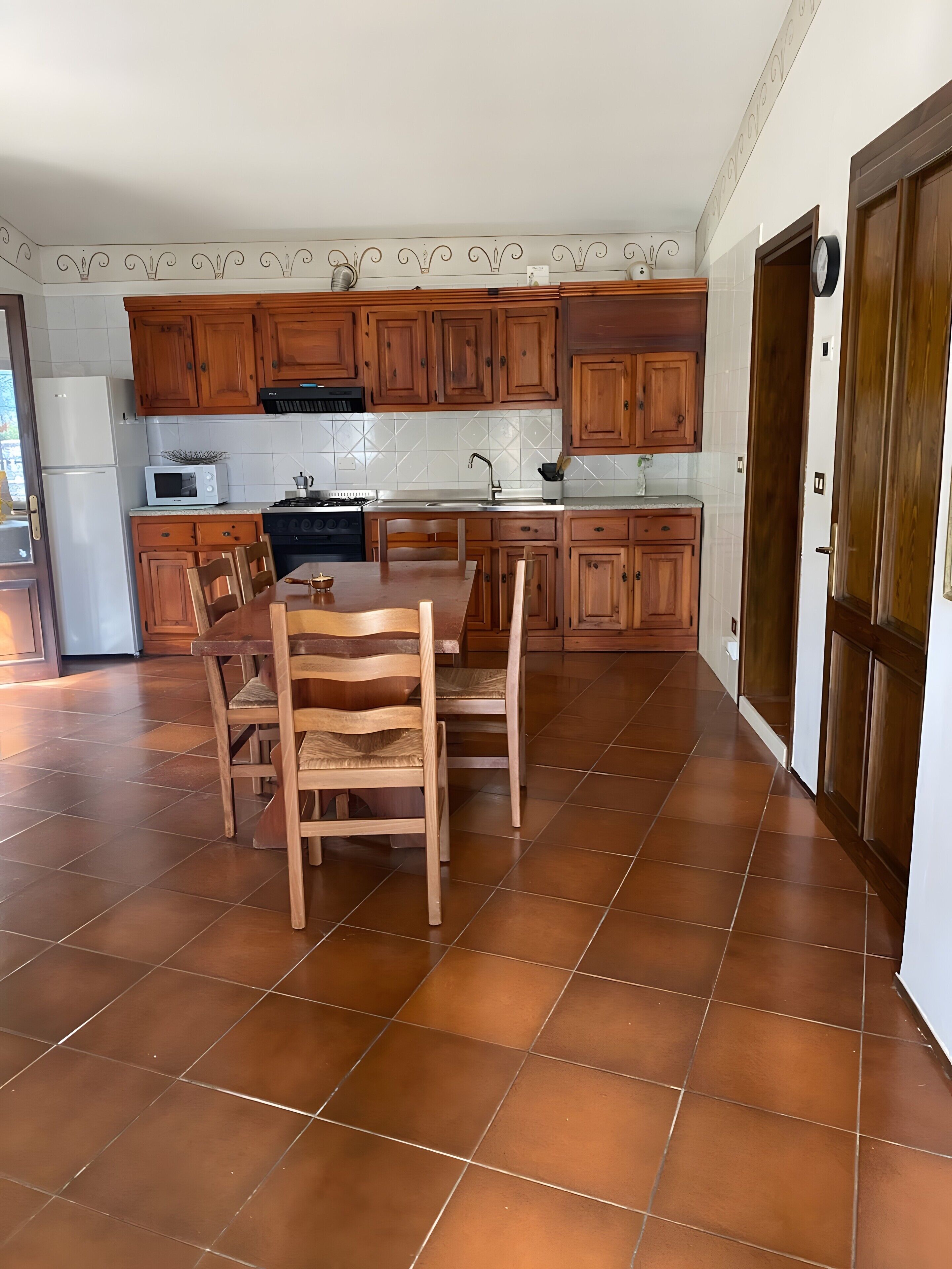 Uma cozinha com armários de madeira, uma mesa de jantar com cadeiras, um micro-ondas e um fogão.