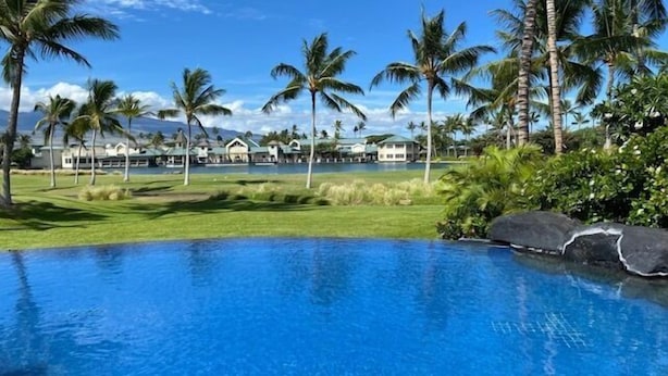 Una piscina con vistas a un resort tropical, palmeras y un cielo despejado.