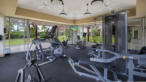 Un gimnasio con máquinas de cardio, equipo de entrenamiento de pesas y una pantalla grande.