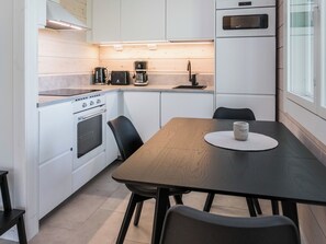 A compact kitchen with a stove, oven, and microwave. There is a dining table with chairs and a coffee maker on the counter.
