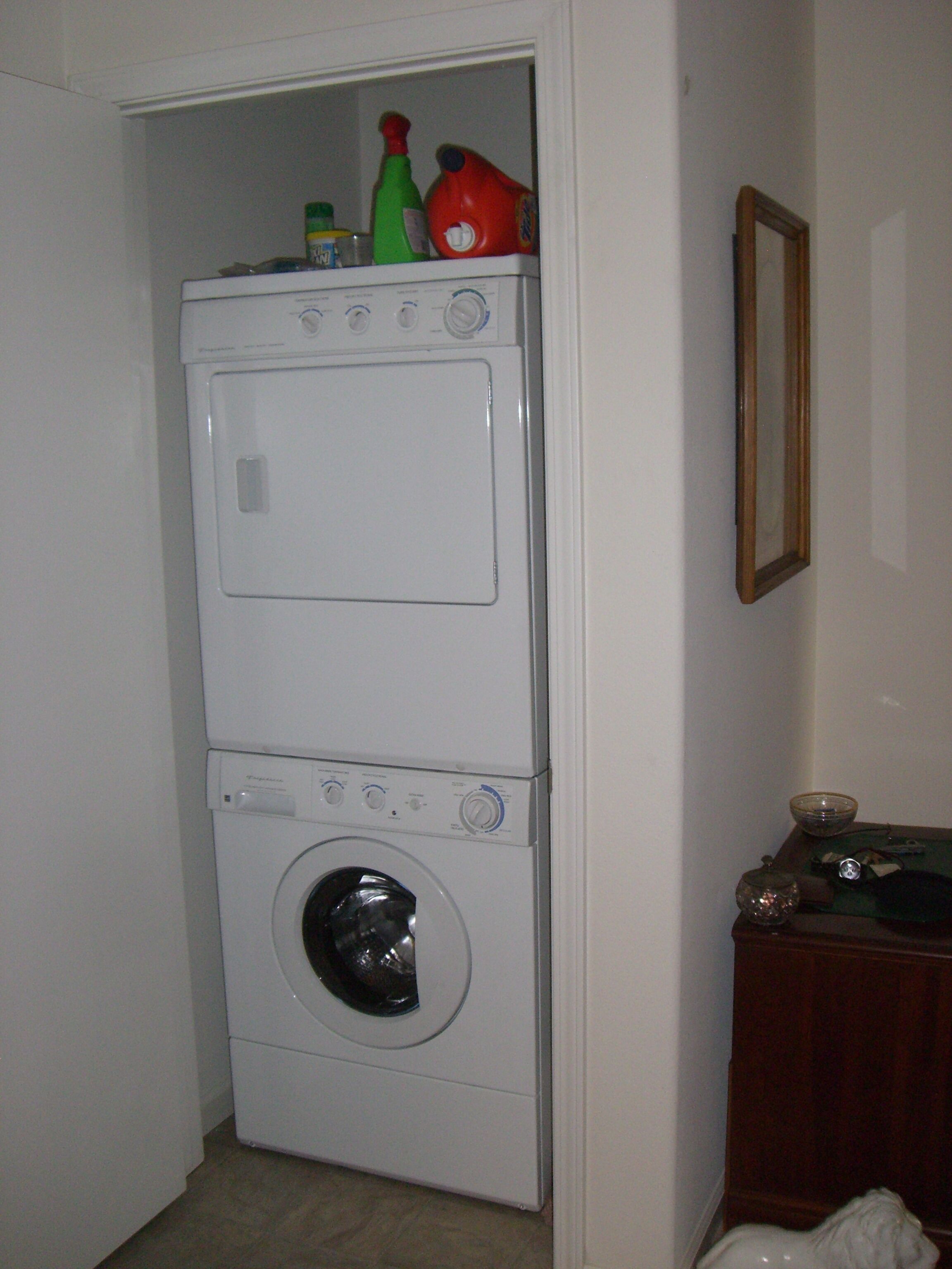 Een gestapelde wasmachine en droger met een plank erboven vol schoonmaakmiddelen.