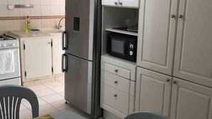Una cocina compacta con refrigerador, microondas y gabinetes blancos. Hay una mesa de comedor con sillas y mantel decorado.