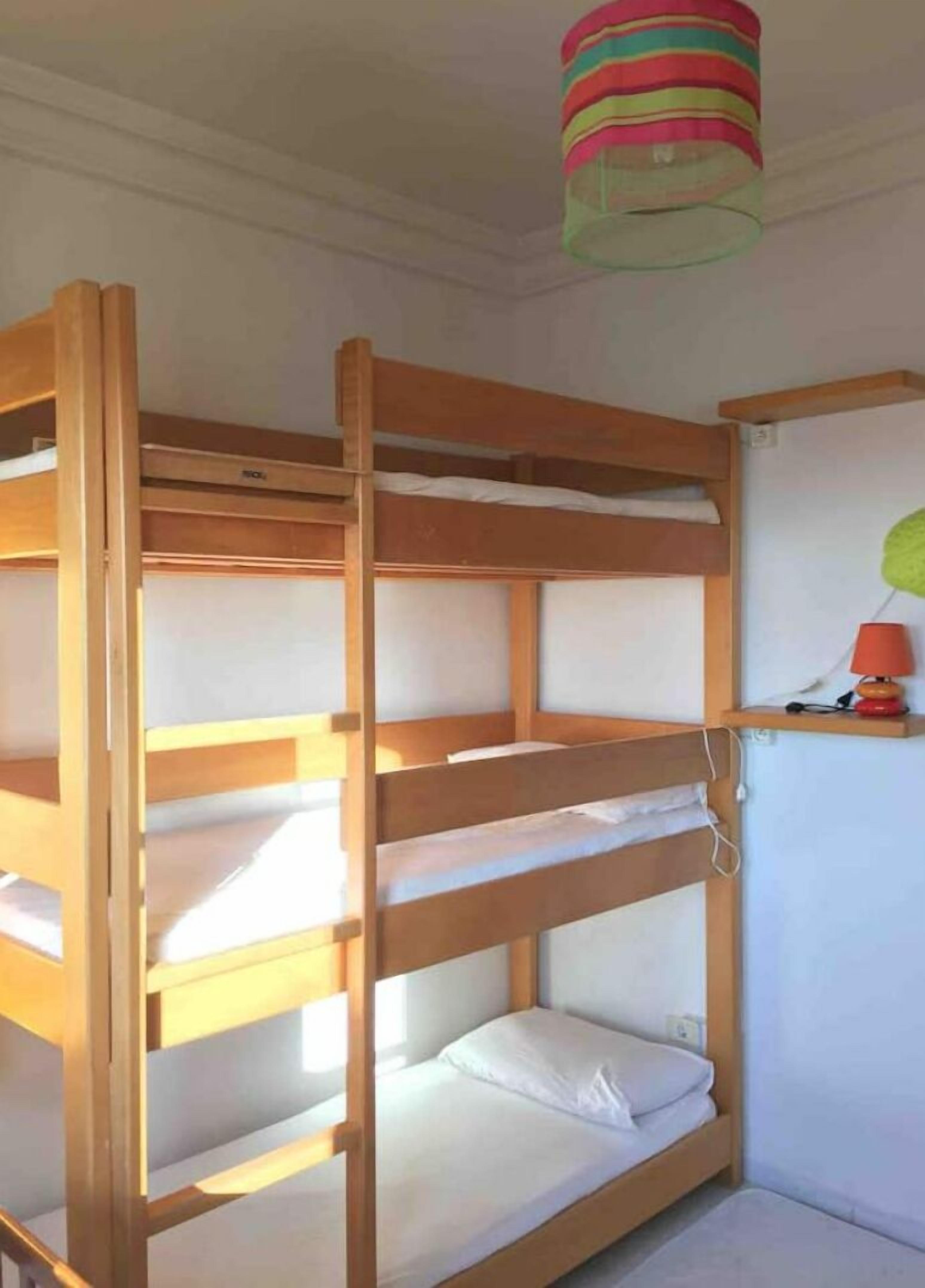 Un lit superposé à trois niveaux, une petite étagère avec une lampe et une lampe suspendue colorée au-dessus.