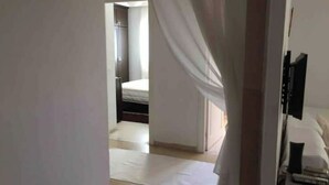 Un dormitorio con cama, mesita de noche y televisor sobre un mueble.