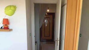 Un pasillo estrecho con una puerta de madera al final, un estante pequeño con una lámpara y un adorno en la pared.