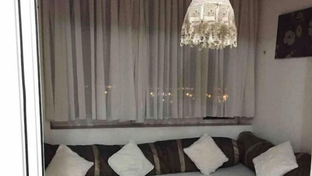 Un rincón acogedor con asientos, un banco acolchado, una lámpara decorativa y cortinas traslúcidas.