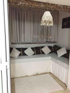 Un coin salon accueillant avec un banc rembourré, un lustre décoratif et des rideaux légers.
