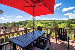 Une terrasse en bois avec une table et des chaises, un parasol rouge et une vue panoramique sur un paysage verdoyant.