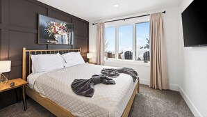 A hotel room with a large bed, a painting on the wall, a window with curtains, and a flat-screen TV.