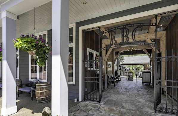 A covered outdoor area with a wooden bench, a hanging flower basket, and a stone pathway leading to a gate with 'BC' above it. - Spacious & Updated Across from Holiday Valley (Ellicottville)