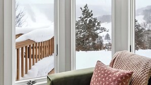 A corner room with large windows, a green sofa, and a patterned pillow.