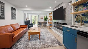 A modern living room with a leather sofa, a wooden coffee table, and a TV in the kitchen area.