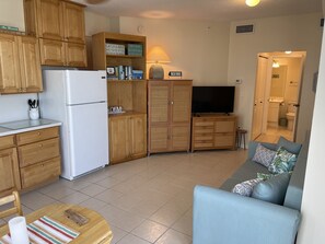 A compact living space with wooden cabinets, a refrigerator, a television, and a sofa.