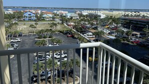 Vista desde un balcón sobre un estacionamiento con varios coches, una playa y edificios al fondo.