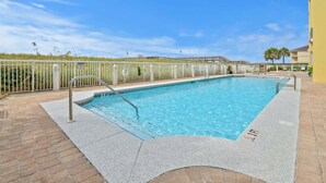 Una piscina rectangular con una escalera metálica, rodeada por una valla blanca y un camino de ladrillo.