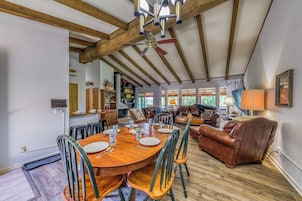 A spacious dining area with a wooden table and chairs, a ceiling fan, and a view of the kitchen and living room.