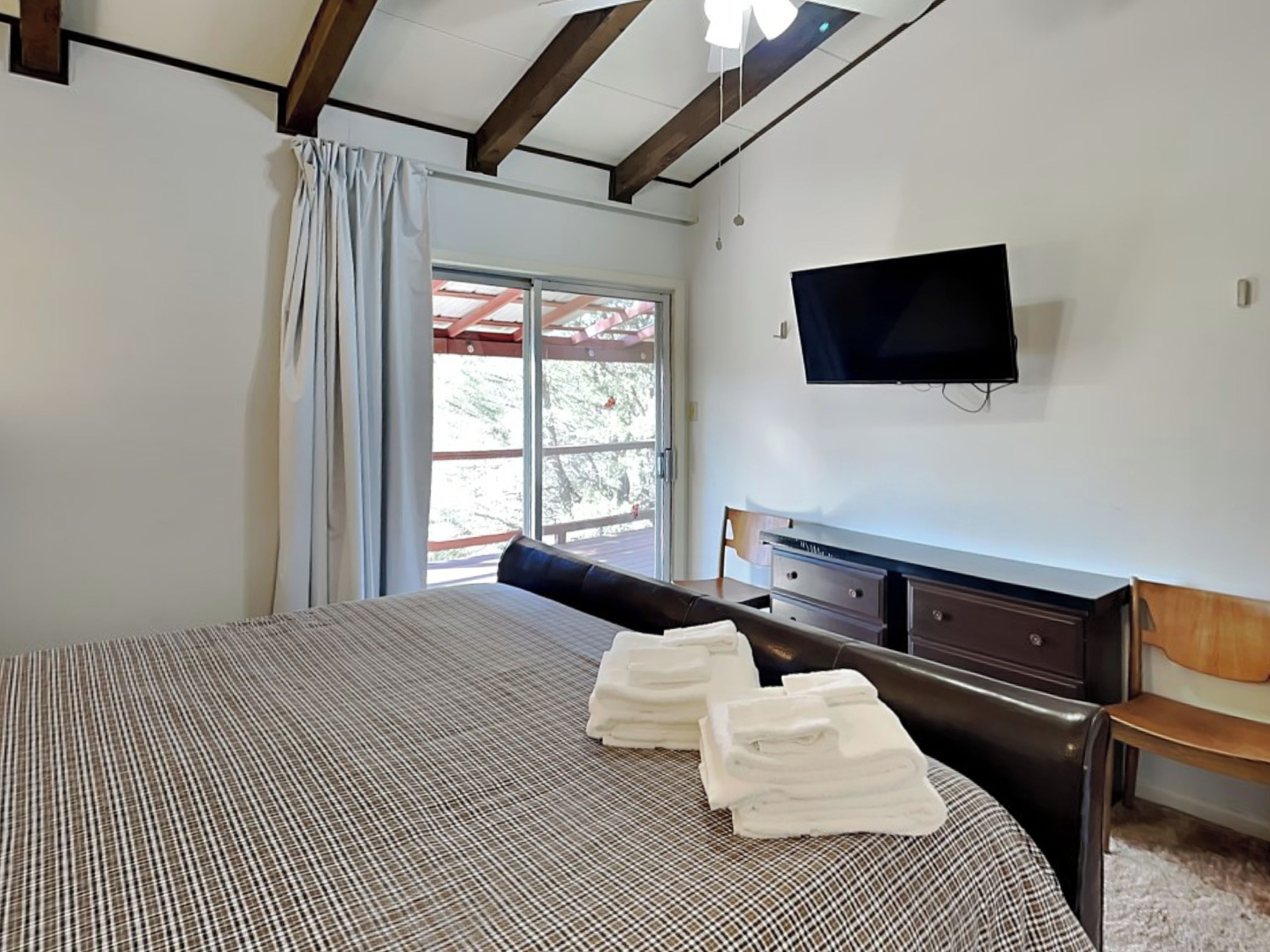 A bedroom with a bed, a dresser, a television, and a window with curtains.